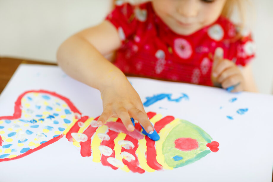 A little girl is painting a fish on a piece of paper.